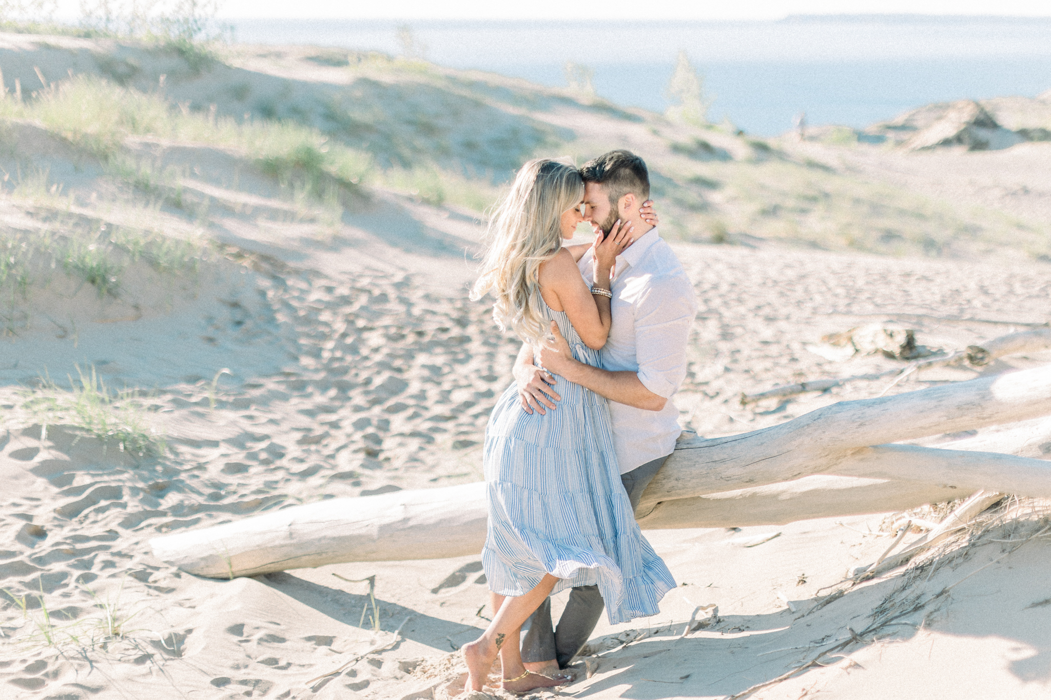 Holly and Tanner embrace beside a driftwood log at Sleeping Bear Dunes, photographed by a Northern Michigan wedding photographer