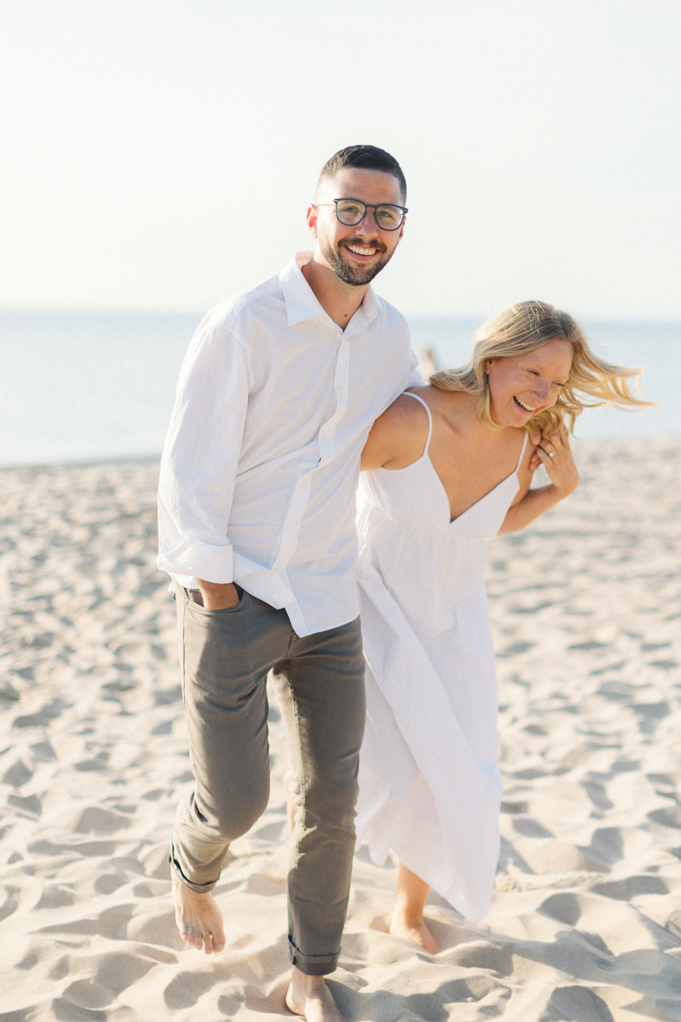 Couple laughing arm in arm on a sandy beach during their Lake Michigan engagement photos