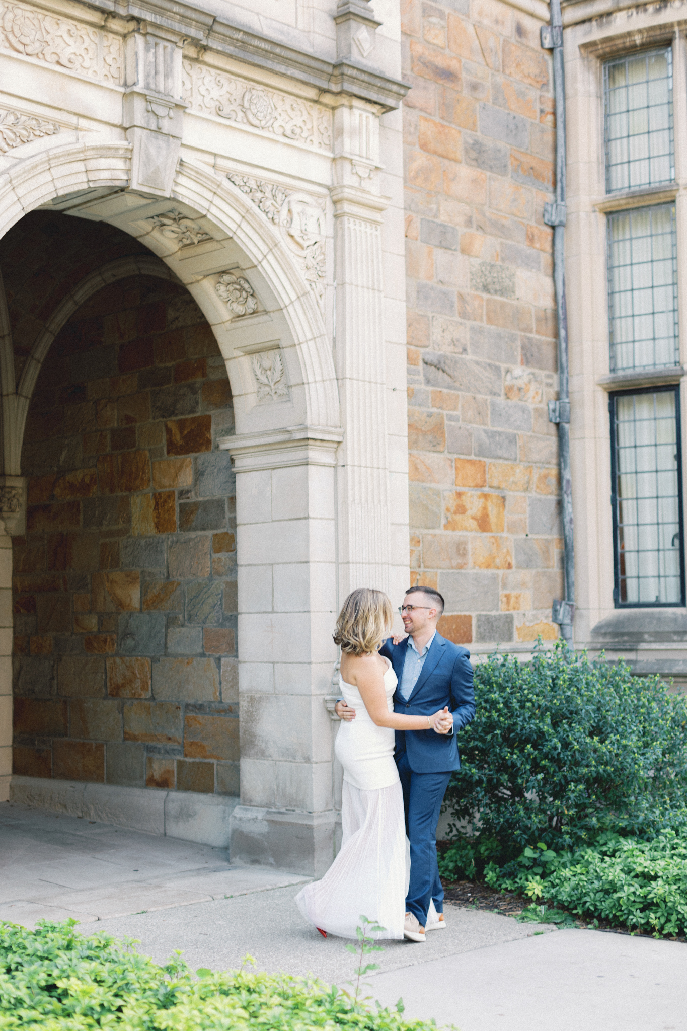 Melissa and David dance beneath a carved stone archway at the University of Michigan Law Quad during their Ann Arbor engagement photos
