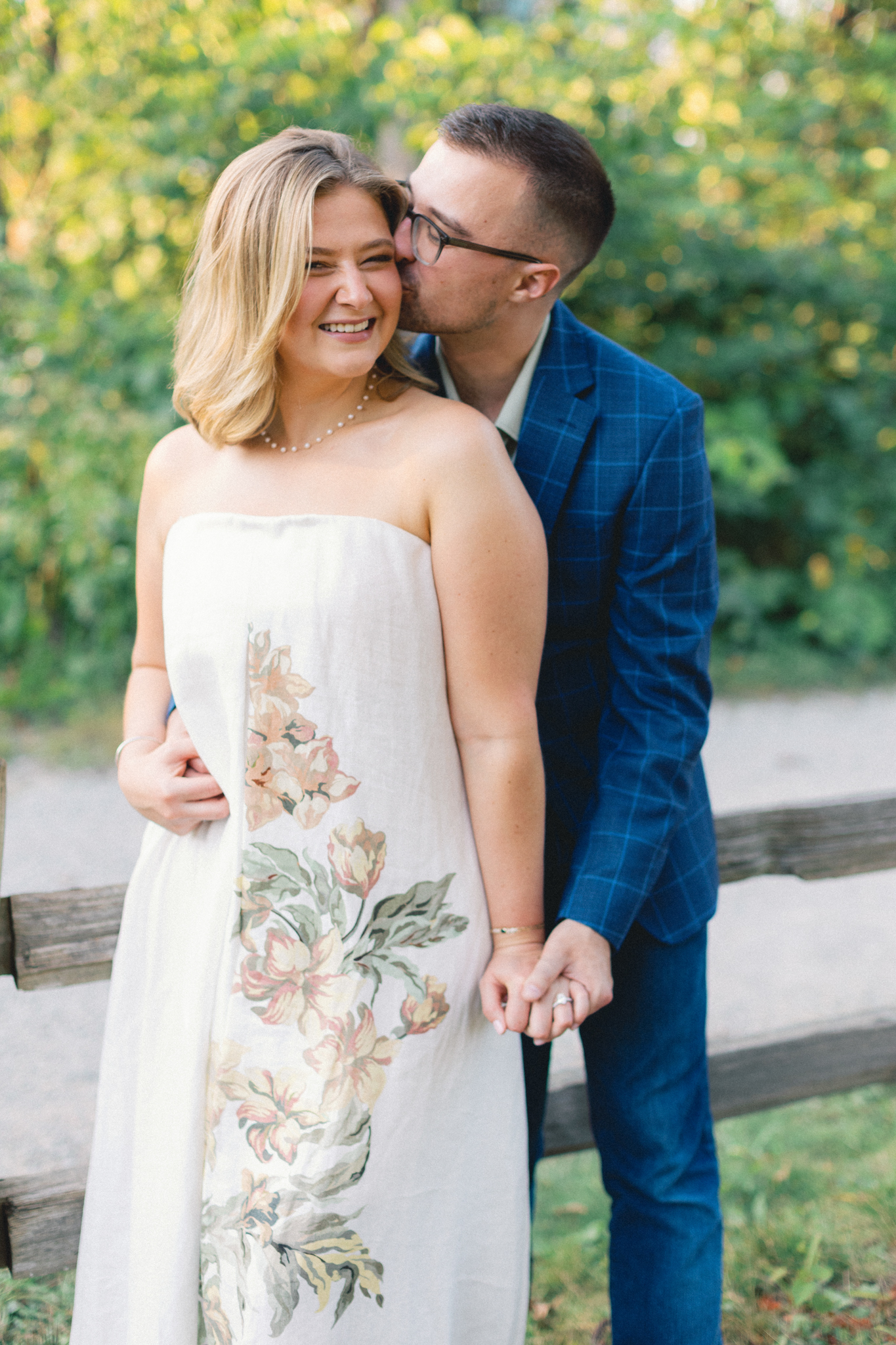 Melissa and David share a kiss beside a split-rail fence at Nichols Arboretum during their Ann Arbor engagement photos