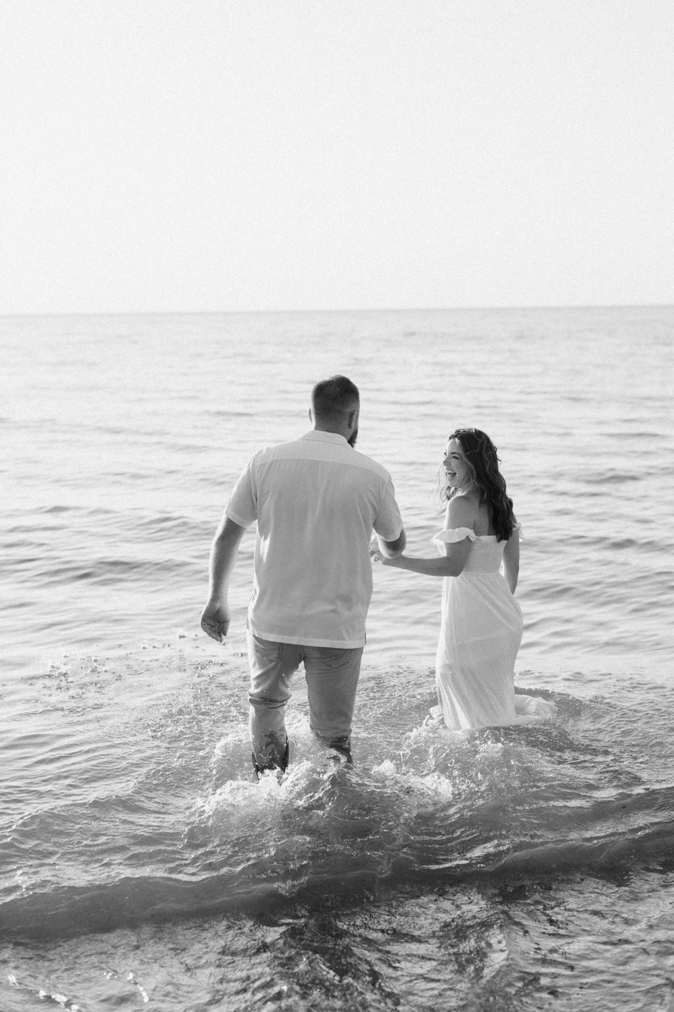 Black and white photo of Liz and Kyle wading into the water at Warren Dunes, one of the best places to take engagement photos in Michigan