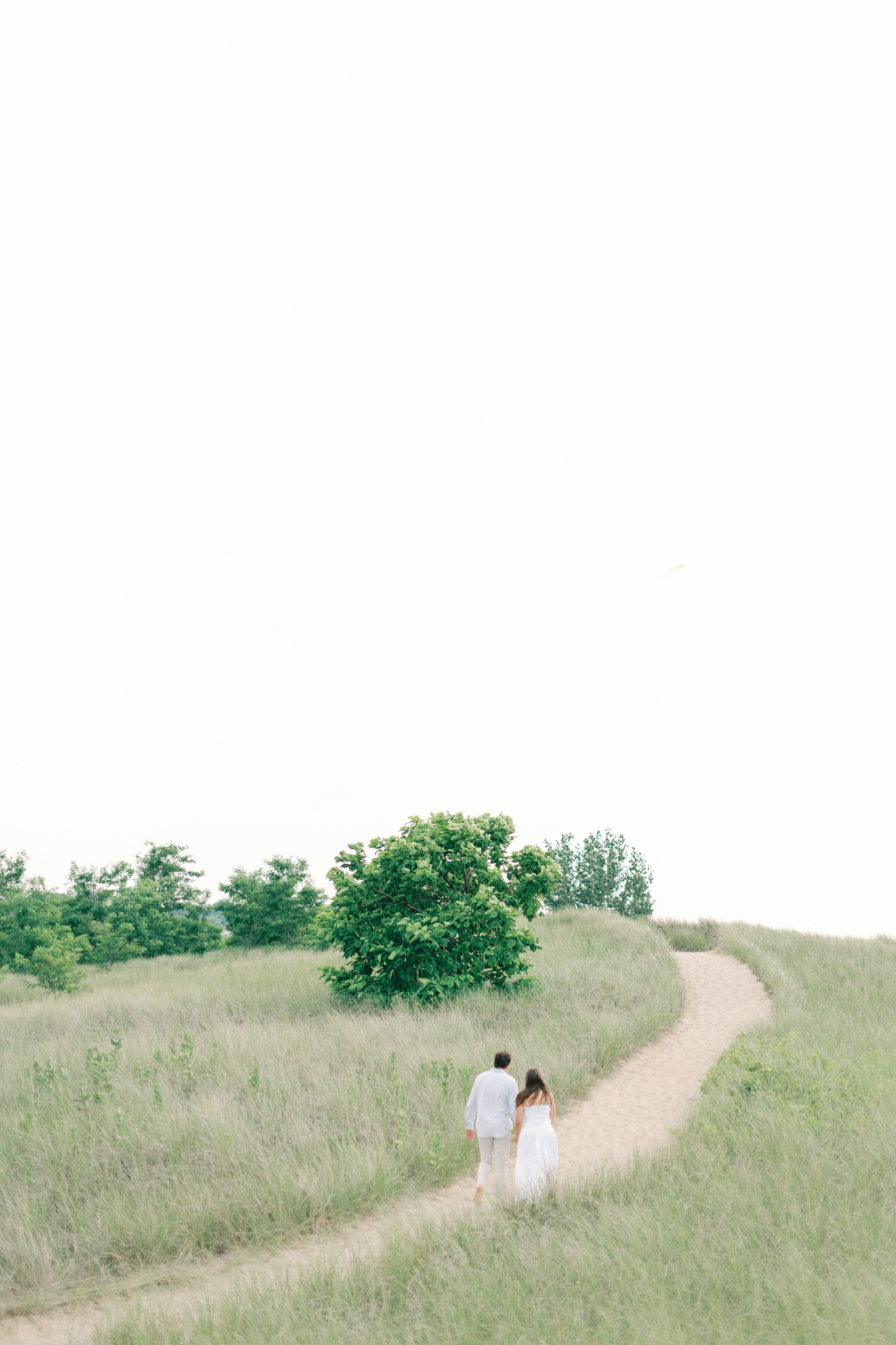 Lauren and Jason walk a sandy dune trail through tall grass during their New Buffalo Michigan engagement photos