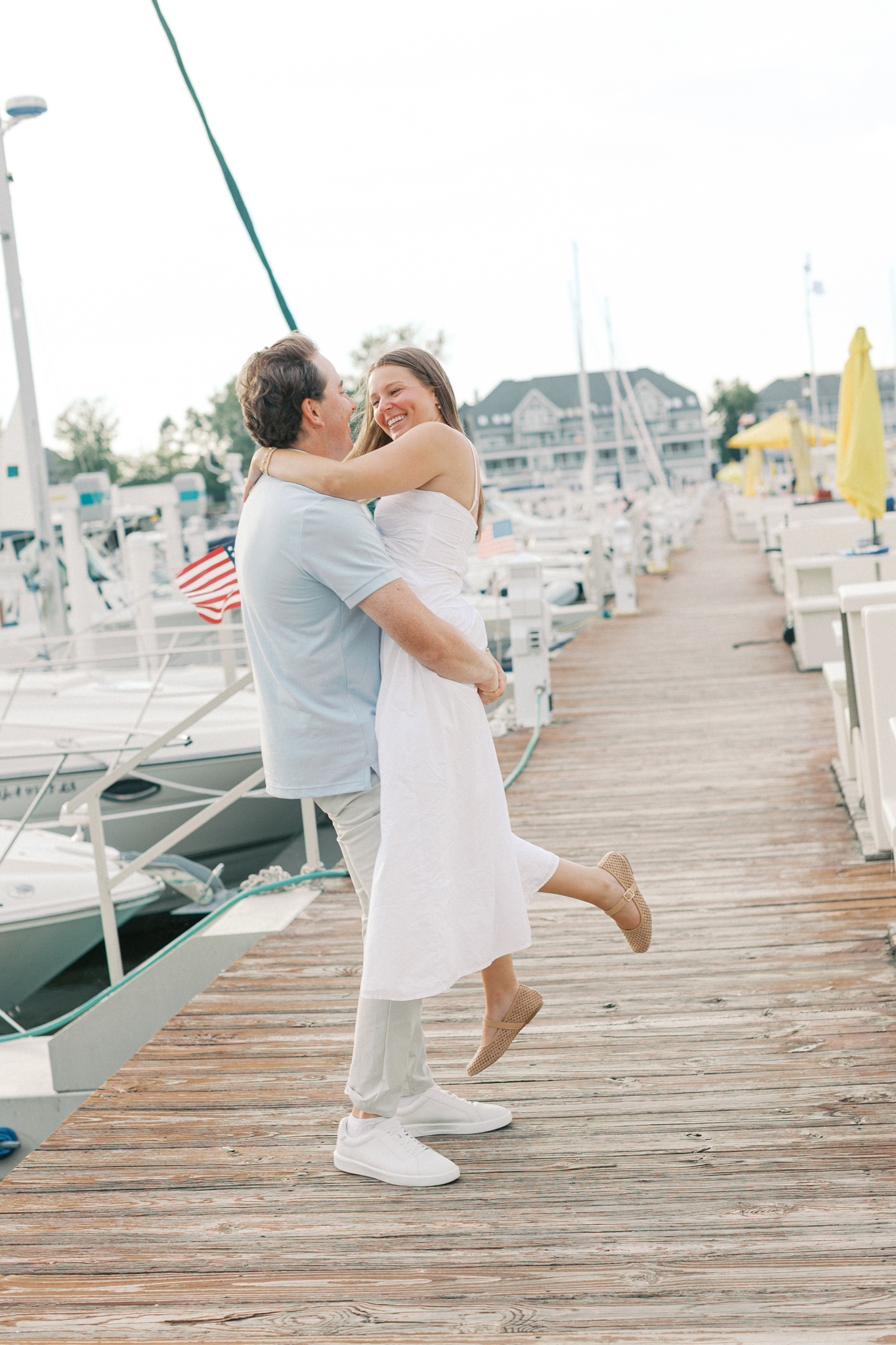 Lauren and Jason laugh together on the marina docks in South Haven, one of the Michigan engagement photo locations for sailboat sessions