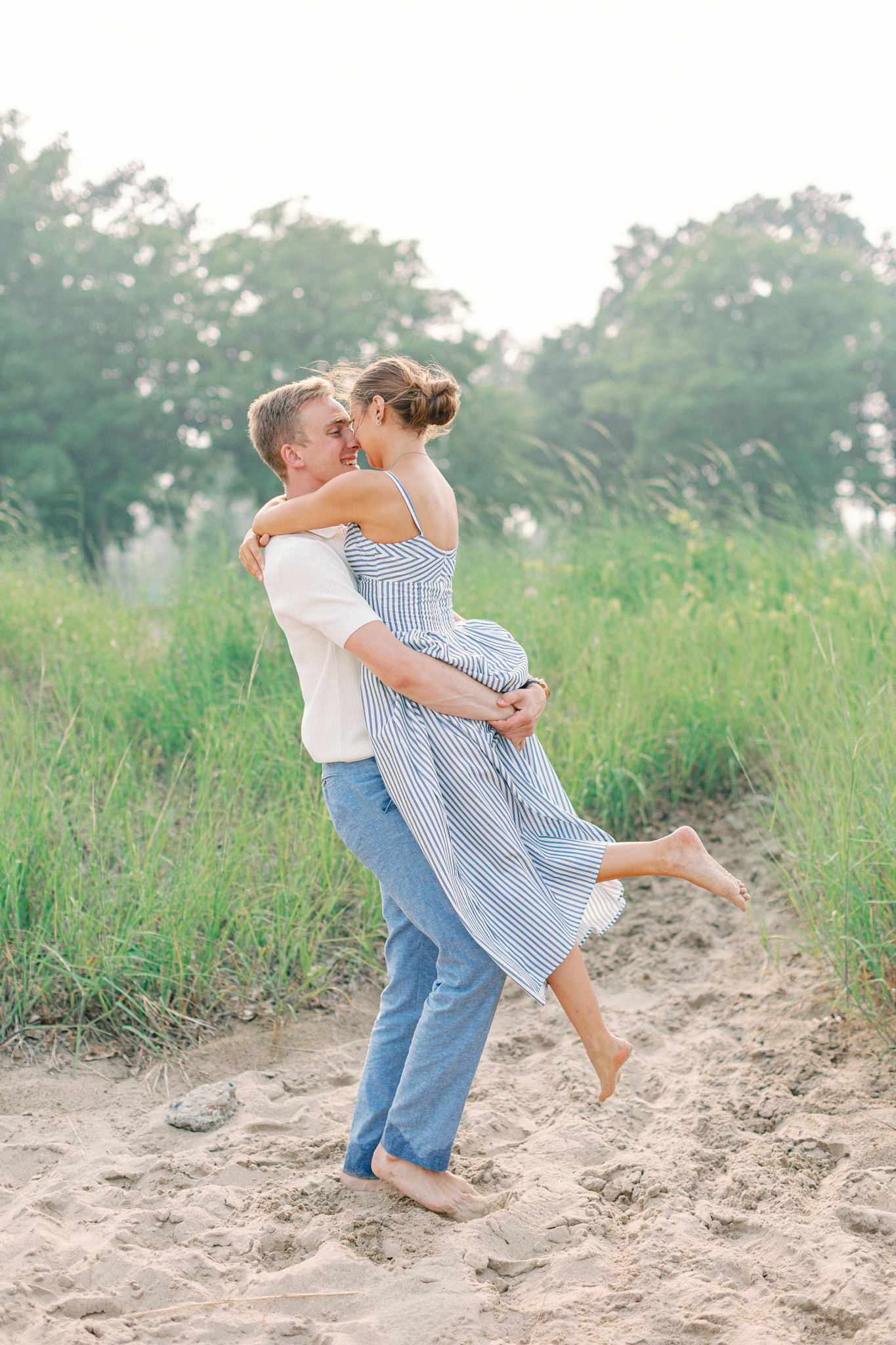 Emma and Caleb embrace in the dune grass along the Lake Huron shoreline during their Michigan engagement pictures in Port Huron
