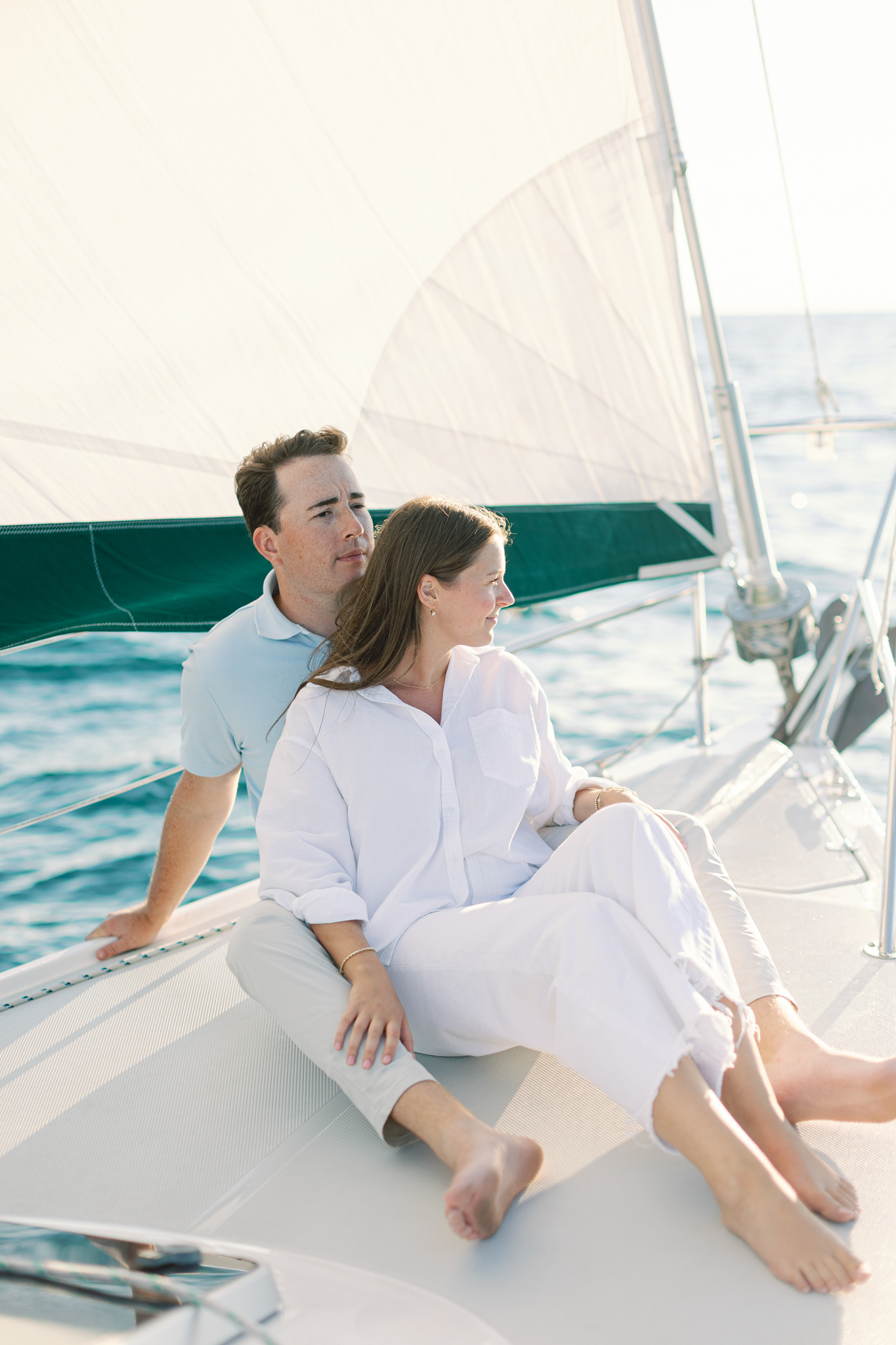 Lauren and Jason sit on the bow of a sailboat under full sail during their Lake Michigan engagement photos near South Haven