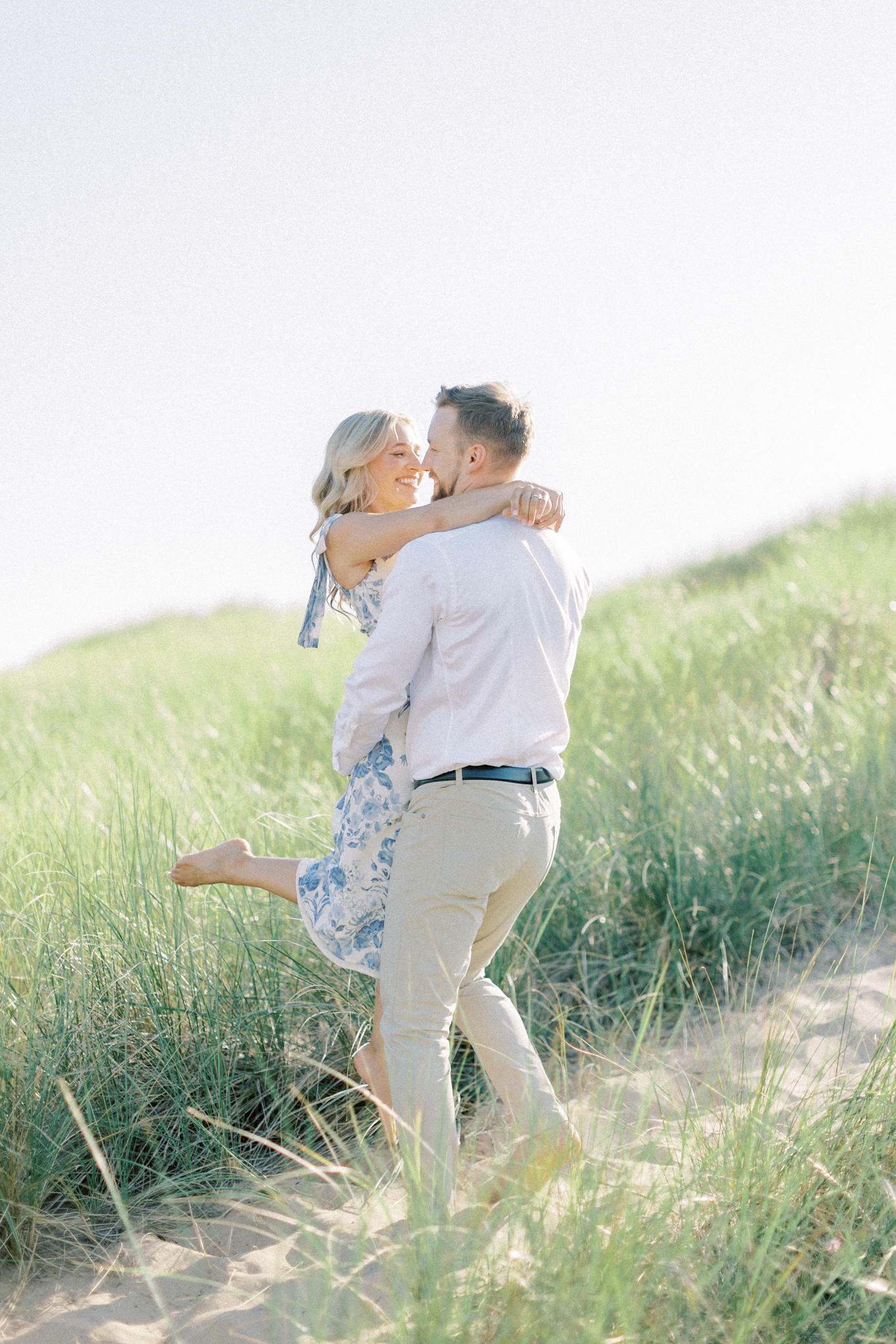 Ashley and Colin embrace in the dune grass at Oval Beach during their West Michigan engagement photos in Saugatuck