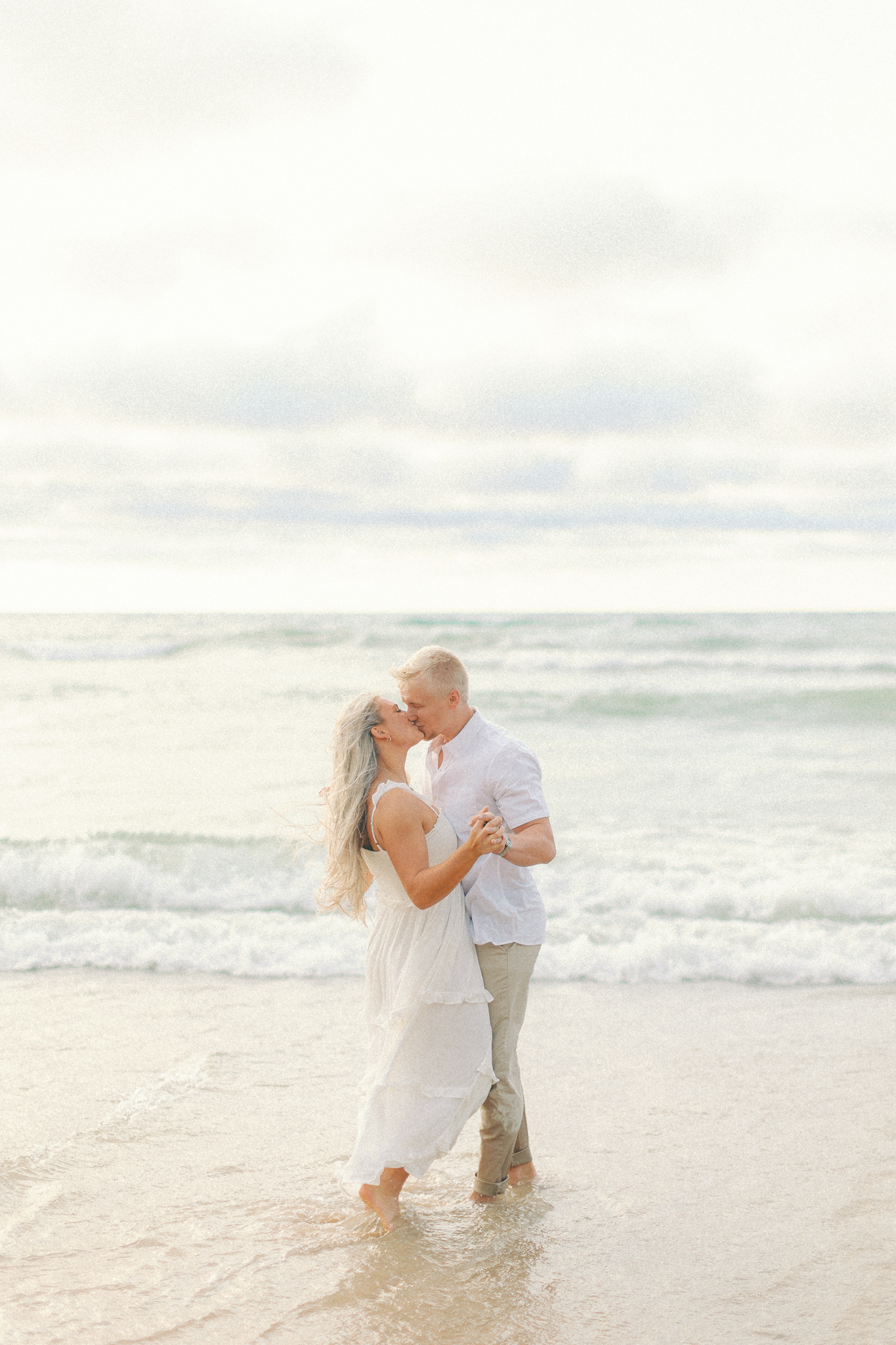 Amber and Adam kiss in the surf at Warren Dunes, one of the best places to take engagement photos in Michigan
