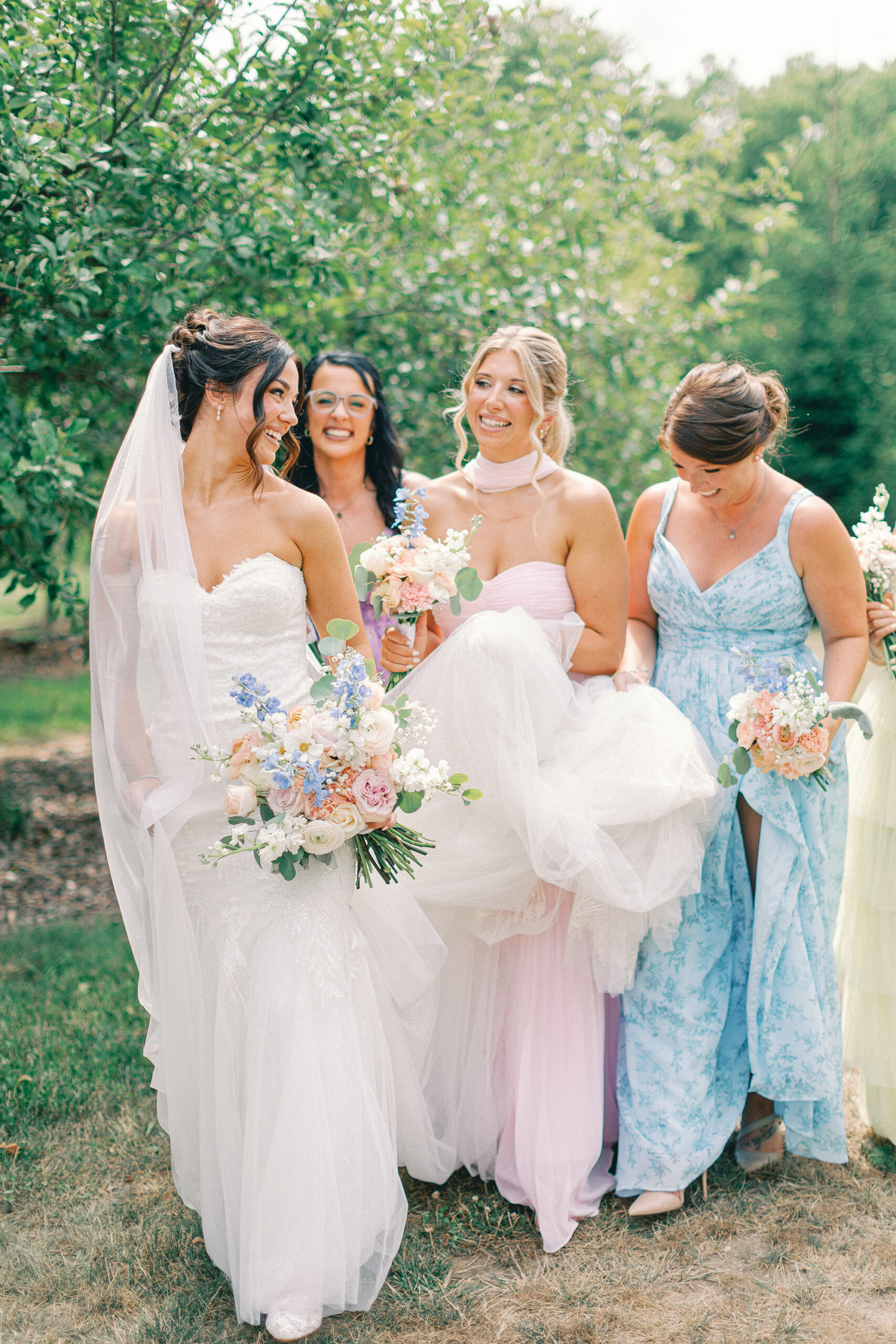 Bride laughing with her bridesmaids in an orchard before a northern Michigan wedding